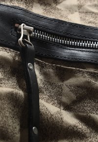 Fermeture éclair en simili cuir noir avec des accessoires en métal argenté sur un fond en tissu beige texturé avec un motif subtil.