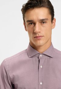 Chemise à carreaux rouge et blanc avec un col classique, fermeture à boutons et tissu lisse. Présente une coupe ajustée avec des motifs subtils.