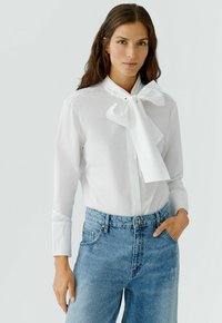 Witte overhemd met een grote strikknopenkraag, lange mouwen, sluiting met knopen aan de voorkant, gecombineerd met hooggesneden lichtblauwe jeans.