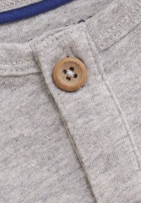 Close-up van een bruine houten knop die is vastgemaakt aan een lichtgrijze gebreide stof met zichtbare stiksels en een blauwe stoffen rand.