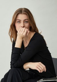 Melna adīta kardigāna ar ribinātiem piedurknēm, apaļa kakla izgriezuma un priekšējiem pogu aizdari, apvienota ar tumšiem biksēm. Gluda tekstūra.