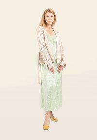 Häkeln Strickjacke in Beige über einem mintgrünen Unterkleid mit Spitzenbesatz, kombiniert mit goldenen Block-Absatz-Mules. Glatte Texturen und fließende Formen.