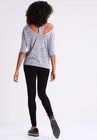 Top gris décolleté avec des manches trois-quarts, présentant un dos découpé, associé à un legging noir et des chaussures à enfiler avec des semelles rayées.
