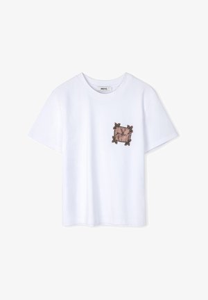 Witte katoenen T-shirt met een kleine, decoratieve patch met een bruine rand en handgeschreven tekst, omrand met versieringen.