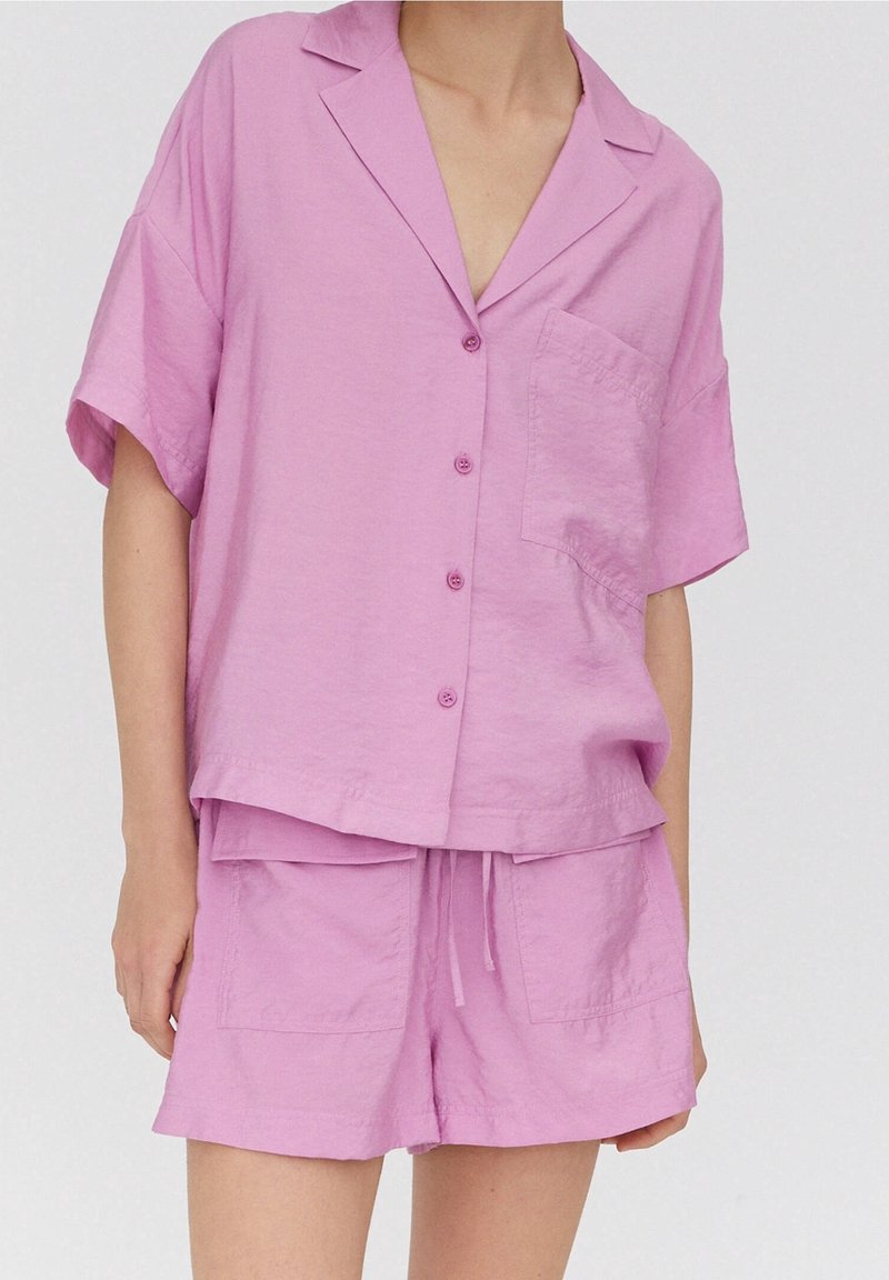 Camisa de botones de manga corta color rosa claro con un bolsillo, combinada con pantalones cortos a juego que tienen cordón y dos bolsillos.