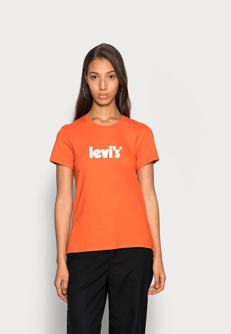 Camiseta de algodón naranja con cuello redondo y mangas cortas, que presenta el logo en blanco de "levi's" centrado en el pecho. Pantalones negros lisos.