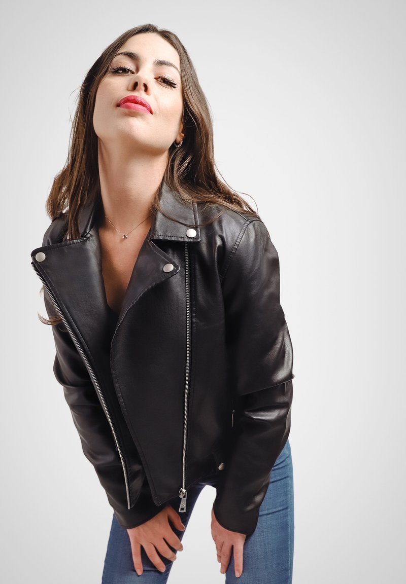Giacca da moto in pelle nera con zip asimmetrica classica, bottoni a scatto e un design aderente, abbinata a jeans in denim blu.