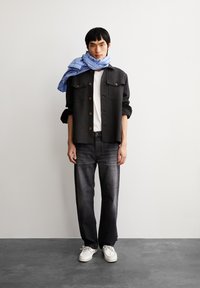 Schwarze, geknöpfte Jacke über einem weißen T-Shirt, graue Jeans und weiße Sneaker. Blau gestreifter Schal um den Hals drapiert. Glatte Texturen.