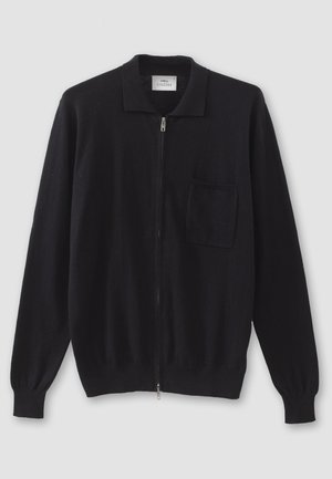 Musta vetoketjullinen neuletakki litteällä kauluksella, pitkät hihat ja yksi rintatasku. Valmistettu pehmeästä, teksturoidusta kankaasta.