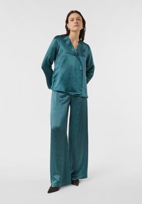 Zweiteiliger Satin-Set in Türkis mit Wickel-Oberteil und langen Ärmeln sowie weiten Hosenbeinen. Glatte Textur mit subtiler Glanzoptik.