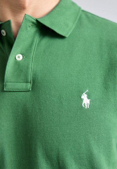 Roheline polo särk, mis on valmistatud tekstuursetest kangast, omab kraed, kolme valget nööpi ja valget broderiat vasakpoolse rinnaga.