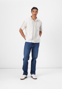 Camisa de manga corta, abotonada, de tela ligera con rayas verticales en tonos pastel. Combinada con unos vaqueros de mezclilla azul y zapatillas blancas.