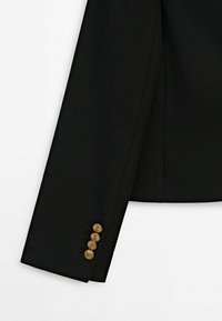 Musta räätälöity takin hiha, jossa on sileä pinta, neljä kultanappia kalvosimessa ja tyylikäs, virtaviivainen muotoilu.