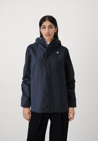 Giacca impermeabile blu marina con cappuccio, chiusura frontale con zip, tasche laterali e un piccolo logo sul petto. Presenta una texture liscia e opaca.