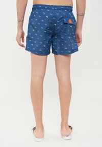 Costume da bagno blu con un design a motivo in verde e azzurro. Presenta una vita elastica e una tasca posteriore con una toppa arancione.