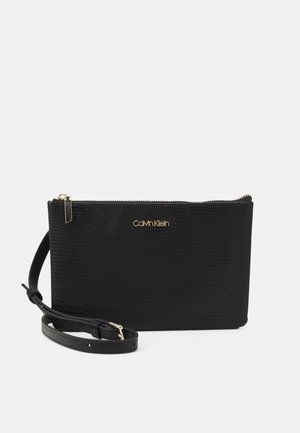 Pochette synthétique noire avec une finition texturée, dotée de quincaillerie dorée et d'une fermeture éclair. Inclut une bandoulière réglable pour le transport.