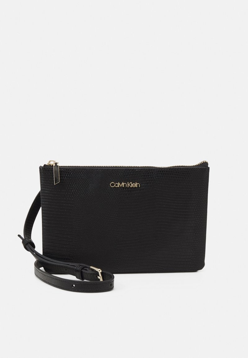 Pochette synthétique noire avec une finition texturée, dotée de quincaillerie dorée et d'une fermeture éclair. Inclut une bandoulière réglable pour le transport.
