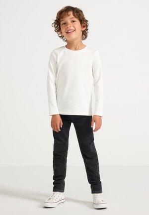 Vit långärmad t-shirt i ribbat tyg, kombinerad med svarta slim-fit jeans och vita sneakers med färgade accenter.