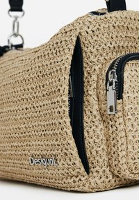 Geflochtene Strohtasche mit schwarzen Reißverschlussakzenten. Verfügt über eine strukturierte Oberfläche, ein Hauptfach und eine vordere Reißverschlusstasche. Silbernes Logo sichtbar.