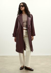 Burgundské kožené trench coat s širokými klopami, double-breasted gombíkmi a bočnými vreckami; kombinované so smotanovými nohavicami a hnedými balerínkami.