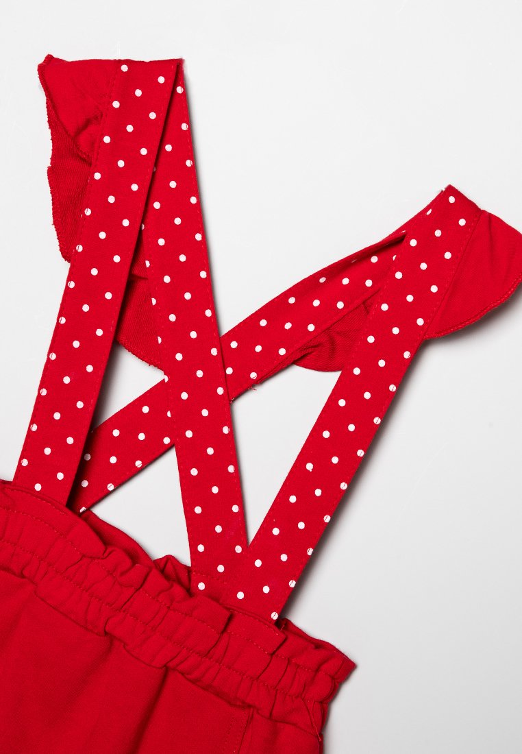 Rote Stoff-Hosenträger mit weißen Polka-Dots, ausgestattet mit einem gerafften Bund und breiten Trägern, die sich am Rücken kreuzen, weiche Textur.