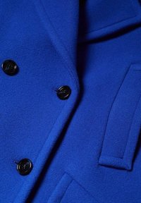 Blauwe wollen jas met een gestructureerde afwerking, zwarte knopen, piekende revers en een zijzakdetail.