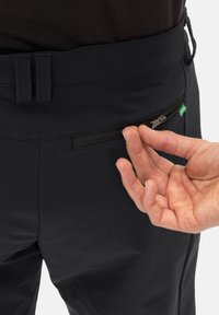 Pantaloni neri con una trama liscia presentano una tasca con zip sulla vita. Una mano viene mostrata mentre utilizza la zip per accedere.