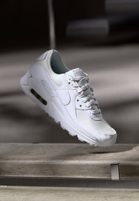 Zapatillas Nike blancas con parte superior de malla y cuero, puntera redonda, cierre con cuerda y amortiguación de aire visible en la suela.