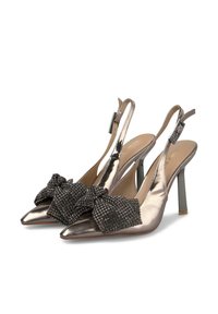 Tacones slingback plateados metálicos con punta afilada, adornados con un lazo negro y acentos brillantes. El diseño de tacón delgado complementa la forma elegante.