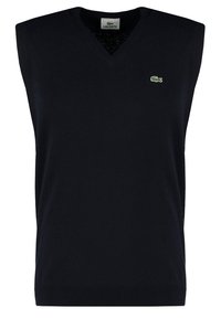 Marinblå ärmlös stickad pullover med V-hals. Har en liten grön krokodillogo på vänster bröst. Ribbat avslut längst ner.