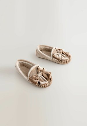 Šviesiai bežinės aksominės šlepetės su puriu kailiu viduje, su dideliu kaspinu akcentu ir taškinėmis tekstūromis ant viršaus. Suapvalinta forma.