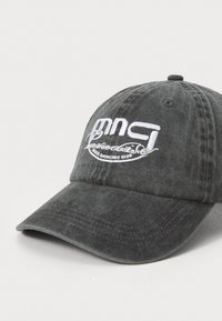 Black denim baseball cap with a curved brim, featuring white embroidered text and a logo on the front. Textured fabric with stitching details.