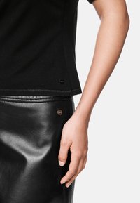 Schwarzes Strickoberteil mit kurzen Ärmeln, kombiniert mit einem schwarzen Lederrock. Verfügt über einen kleinen metallischen Akzent am Saum und hat eine glatte Textur.