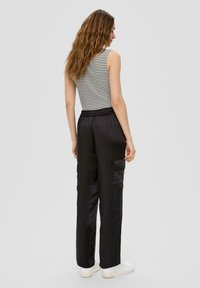 Zwarte cargo broek met een elastische tailleband, zijkanten zakken en een soepele textuur, gecombineerd met een gestreepte mouwloze top in een casual pasvorm.
