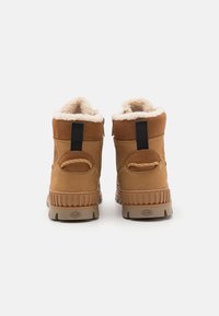 Bottes imperméables marron avec une doublure en fourrure douce, semelles en caoutchouc robustes et languettes noires. Tige en cuir texturé et en daim avec une poignée à l'arrière.