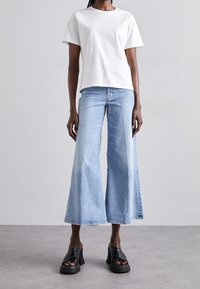 Camiseta blanca de algodón, ajuste relajado, combinada con jeans de mezclilla de pierna ancha en azul claro. Sandalias de plataforma negras con parte superior texturizada y tacón grueso.