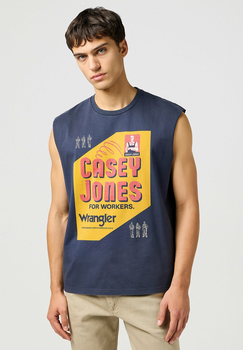 Marinblå ärmlös t-shirt med en stor gul och rosa grafik som står "CASEY JONES FOR WORKERS" och Wrangler-logotypen längst ner.
