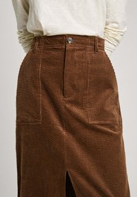 Gonna in velluto a coste marrone con rigature verticali, dotata di spacco frontale, chiusura con bottoni e due tasche anteriori.