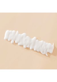 Crème blanche mousseuse tourbillonnée en une ligne horizontale sur une surface beige lisse.