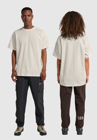 Hvid bomulds t-shirt med korte ærmer og rund hals, vist foran og bagpå af to modeller, der bærer cargo bukser og vandrestøvler.