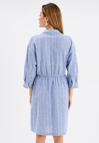 Blau gestreiftes Kleid mit Kragen, langen Ärmeln, elastischem Bund und mittellangem Schnitt. Hergestellt aus einem weich strukturierten Stoff.