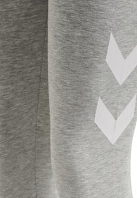 Grå sweatpants i texturerat tyg, med vita chevronmönster på sidan. Designen är enkel och avslappnad.
