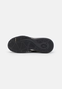Schwarze Gummisneaker-Sohle mit strukturiertem Grip und geometrischem Muster sowie verstärktem Fersenbereich. Flexibles Design für Komfort und Traktion.