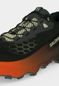 Μαύρο και πορτοκαλί παπούτσι Salomon για τρέξιμο σε μονοπάτια με μοτίβο πάνω μέρος, γρήγορο σύστημα κορδονιών και υφή στη σόλα για καλύτερη πρόσφυση.
