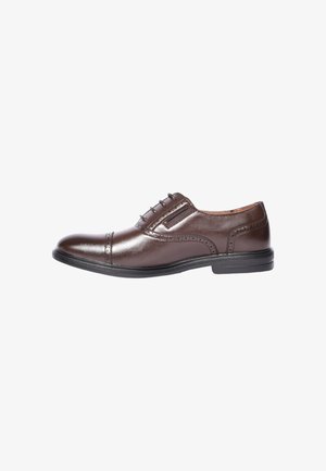 Scarpa da uomo in pelle marrone con punta a cappuccio, dettagli brogue, suola nera e pannelli elastici laterali, vista dal lato esterno.