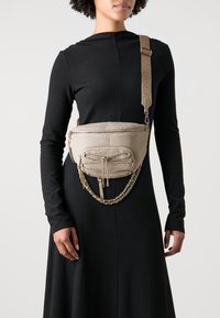 Beige gewebte Schultertasche mit einem Reißverschlussfach auf der Vorderseite und Kettenakzenten, ausgestattet mit einem verstellbaren Tragegurt und strukturiertem Stoff.