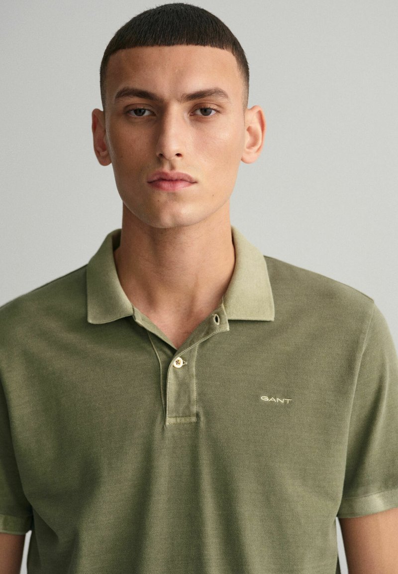 Polo vert avec un design à col, présentant un tissu texturé, deux boutons et un petit logo brodé sur la poitrine.