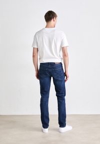 Kék farmernadrág, slim fit szabású, standard zsebekkel és közepes derékmagassággal. Egyszerű, fehér, rövid ujjú pólóval és fehér sportcipővel párosítva.