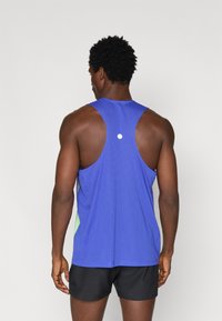 Μπλε αθλητική αμάνικη μπλάντα με υφασμάτινο σχέδιο, στρογγυλή λαιμόκοψη και σχέδιο ράχης ράλι. Διαθέτει λευκή τονισμένη λεπτομέρεια. Φοράει μαύρες βερμούδες.