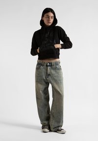 Černá zkrácená mikina s grafickým potiskem, v kombinaci se světle modrými širokými džíny. Model má na sobě černé sneakers, což vytváří uvolněný vzhled.